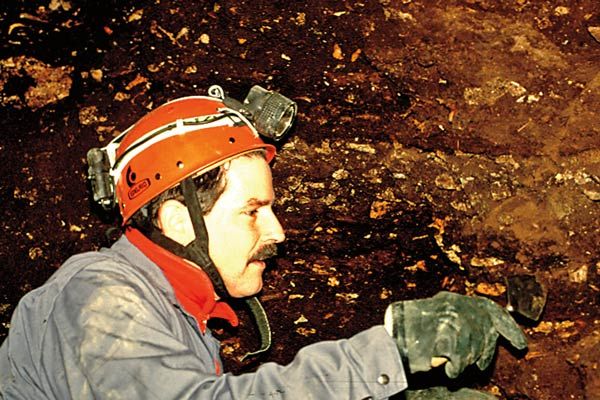 Paleontologist excavating the Bone Bed deposit inside Rat's Nest Cave, Canmore Alberta — stratigraphic record of Bow Valley wildlife spanning 7000 years in the Canadian Rockies